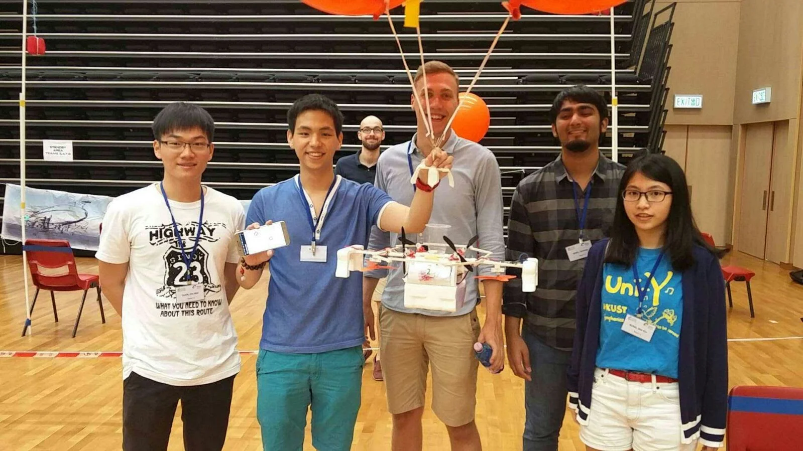 A project team at HKUST displaying a flying prototype in a sports hall.